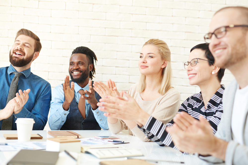 5 employees sitting at a table and clapping