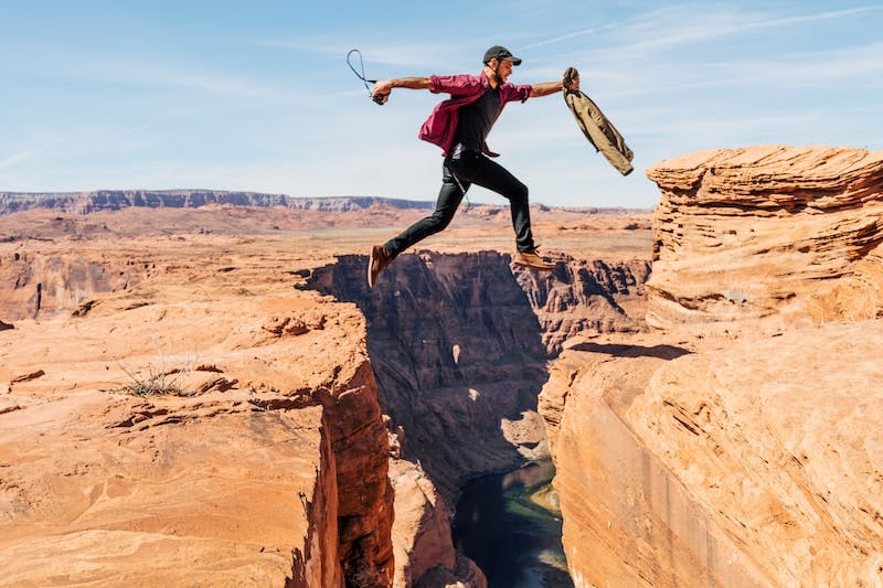 man with courage jumping over a very wide crevice in a cliff.